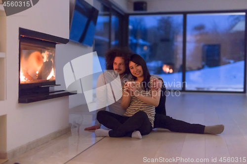 Image of happy multiethnic couple sitting in front of fireplace