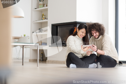 Image of multiethnic couple using tablet computer in front of fireplace