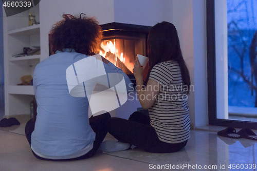 Image of happy multiethnic couple sitting in front of fireplace