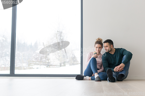 Image of young couple sitting on the floor near window at home
