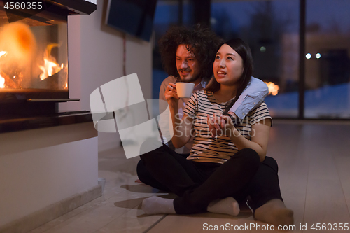 Image of happy multiethnic couple sitting in front of fireplace