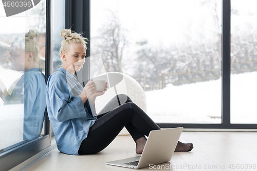 Image of woman drinking coffee and using laptop at home