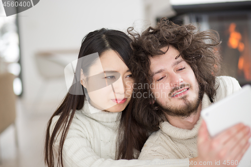 Image of multiethnic couple using tablet computer in front of fireplace