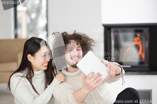 Image of multiethnic couple using tablet computer in front of fireplace