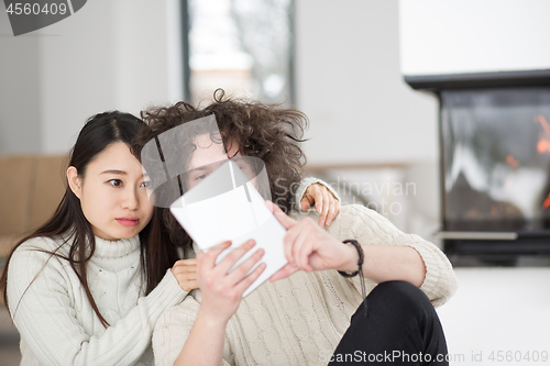 Image of multiethnic couple using tablet computer in front of fireplace