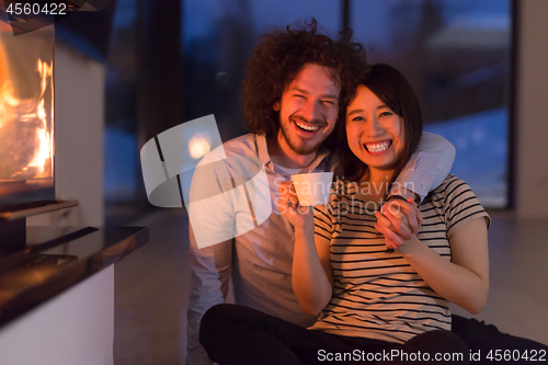 Image of happy multiethnic couple sitting in front of fireplace