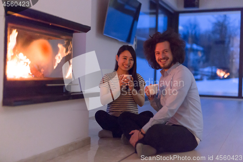 Image of happy multiethnic couple sitting in front of fireplace