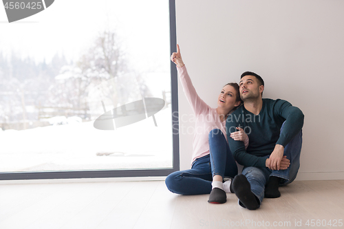 Image of young couple sitting on the floor near window at home