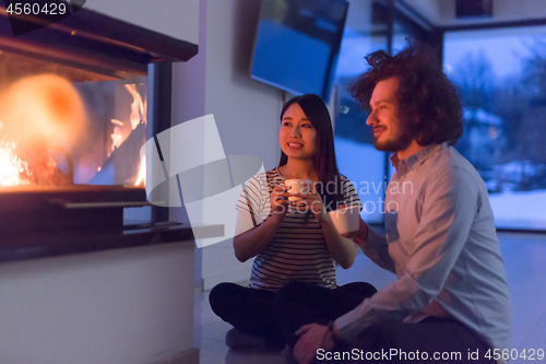 Image of happy multiethnic couple sitting in front of fireplace