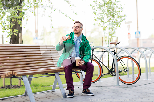 Image of young man or hipster with coffee eating sandwich