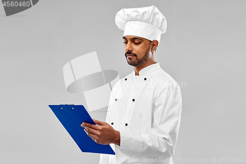 Image of male indian chef reading menu on clipboard