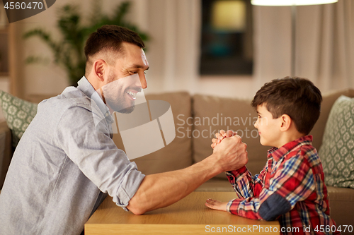 Image of happy father and little son arm wrestling at home