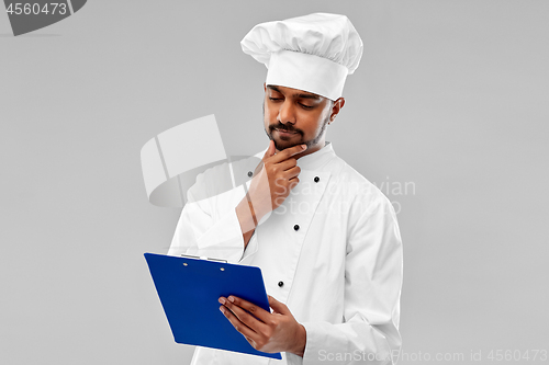 Image of male indian chef reading menu on clipboard