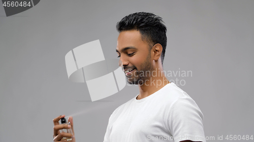 Image of happy indian man with perfume over grey background