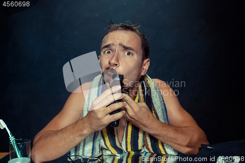 Image of young man in bedroom sitting in front of the mirror scratching his beard