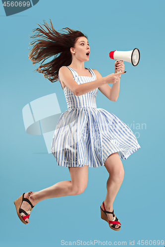 Image of Beautiful young woman jumping with megaphone isolated over blue background