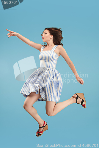 Image of Freedom in moving. Pretty young woman jumping against blue background