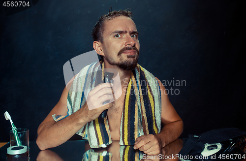 Image of young man in bedroom sitting in front of the mirror scratching his beard