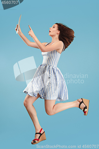 Image of Image of young woman over blue background using laptop computer or tablet gadget while jumping.