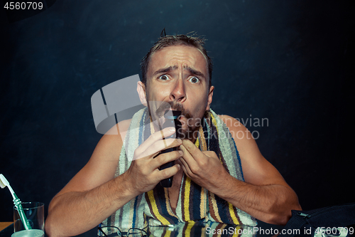 Image of young man in bedroom sitting in front of the mirror scratching his beard