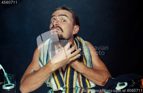 Image of young man in bedroom sitting in front of the mirror scratching his beard