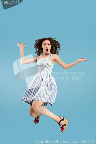 Image of Freedom in moving. Pretty young woman jumping against blue background