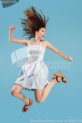 Image of Freedom in moving. Pretty young woman jumping against blue background