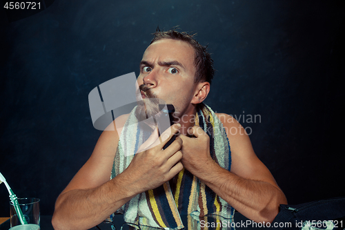 Image of young man in bedroom sitting in front of the mirror scratching his beard