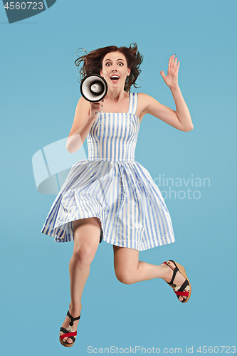 Image of Beautiful young woman jumping with megaphone isolated over blue background