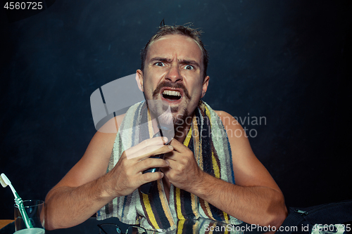 Image of young man in bedroom sitting in front of the mirror scratching his beard