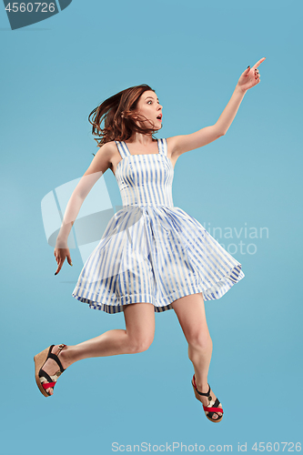 Image of Freedom in moving. Pretty young woman jumping against blue background