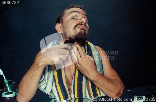 Image of young man in bedroom sitting in front of the mirror scratching his beard