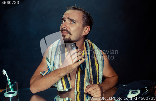 Image of young man in bedroom sitting in front of the mirror scratching his beard