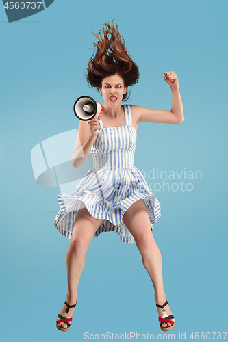 Image of Beautiful young woman jumping with megaphone isolated over blue background