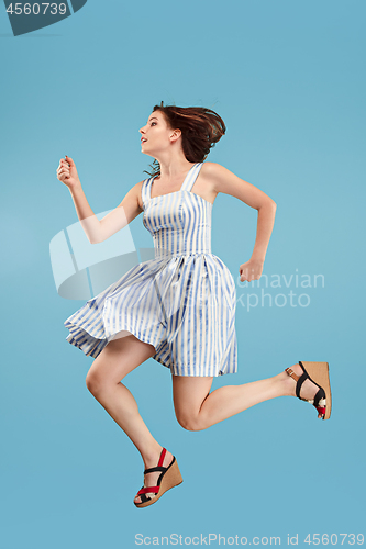 Image of Freedom in moving. Pretty young woman jumping against blue background