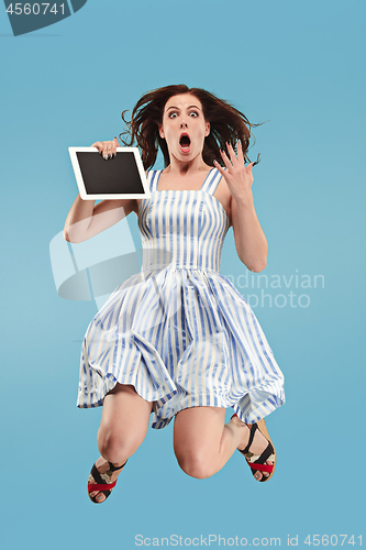 Image of Image of young woman over blue background using laptop computer or tablet gadget while jumping.