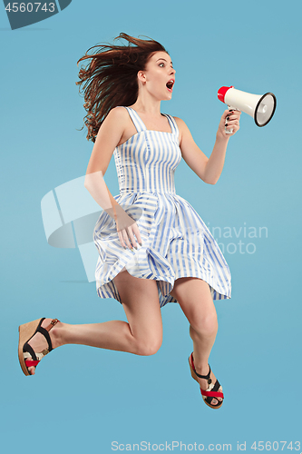 Image of Beautiful young woman jumping with megaphone isolated over blue background