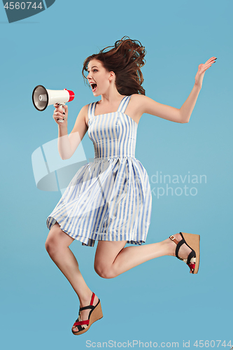 Image of Beautiful young woman jumping with megaphone isolated over blue background