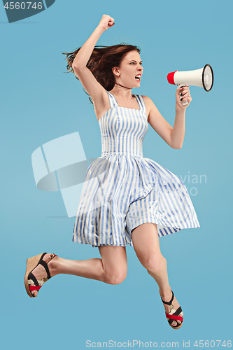 Image of Beautiful young woman jumping with megaphone isolated over blue background