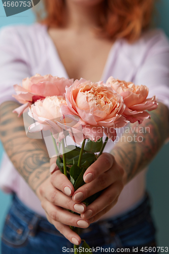 Image of A woman with a tattoo holding delicate pink roses in her hands on a blue background with copy space for text. Holiday gift