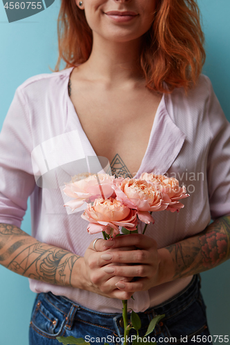 Image of A bouquet of pink roses is holding in hands a sexy red-haired girl around a blue background with copy space. Valentine\'s day concept