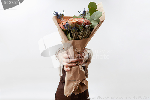 Image of Lady\'s hands hold a nice bouquet from fresh fragrant flowers living coral colored roses on a light background. Copy space. Greeting card for Mother\'s Day.