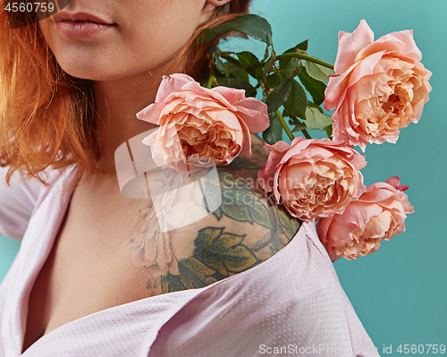 Image of Young cute girl with tattoo on her shoulders and a bouquet of coral roses on a blue background. Postcard to Mother\'s day.