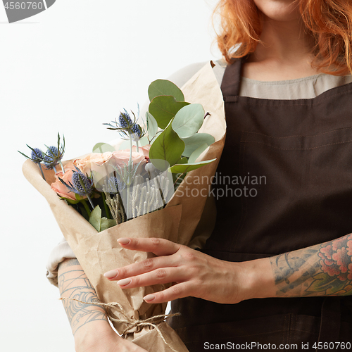 Image of Young girl with ginger hair hold beautiful bunch with fresh natural flowers and leaves on a light background, copy space. Holiday card.