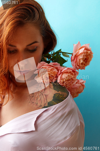 Image of Attractive girl with tattoo on her shoulders and bouquet of coral roses on a blue background, place for text. A gift for Mother\'s Day.