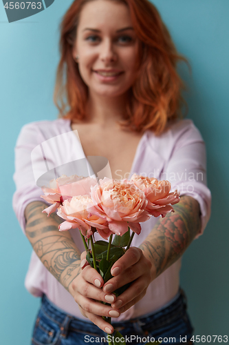 Image of A smiling girl with a tattoo gives a bouquet of pink roses around a blue background with copy space. Mother\'s Day Gift