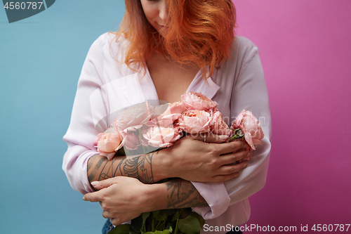 Image of Beautiful red-haired woman with tattoo and bouquet of pink flowers on a double blue-pink background with copy space. Women\'s Day