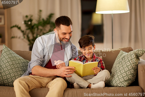 Image of happy father and son reading book sofa at home