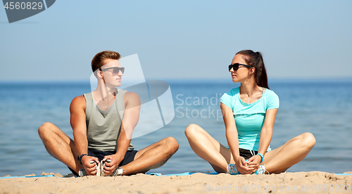 Image of smiling couple stretching legs on beach