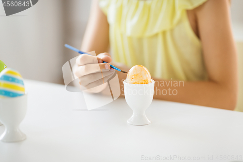 Image of close up of girl coloring easter egg by paintbrush